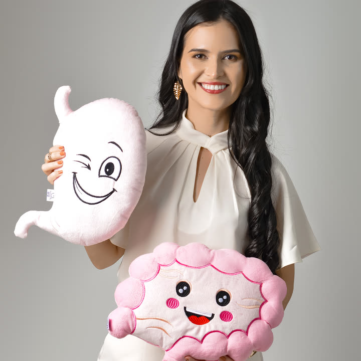 Dra. Thamires Mattos sorrindo, segurando pelúcias em forma de estômago e intestino